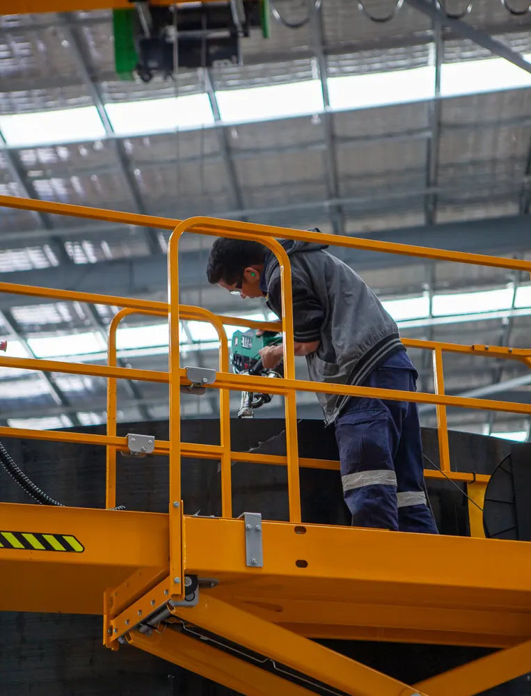 man on elevated work platform holding an extrusion welding gun, welding an HDPE tank lid